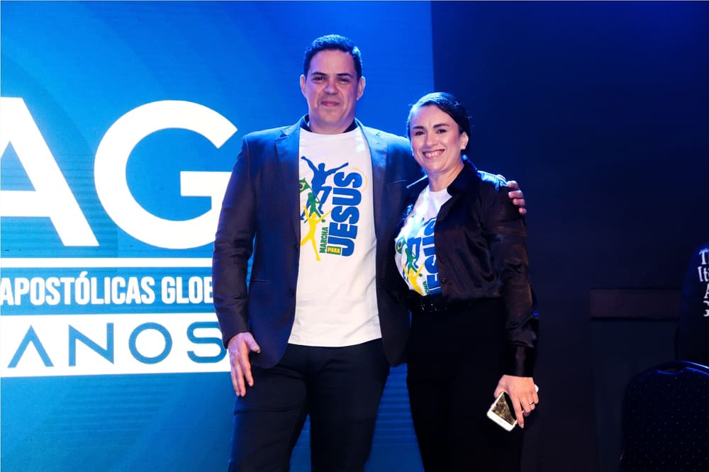 Pr. German Yaku e Pra. Patrícia Yakubisin no palco do evento da CIEAG, com o painel de 18 anos ao fundo.