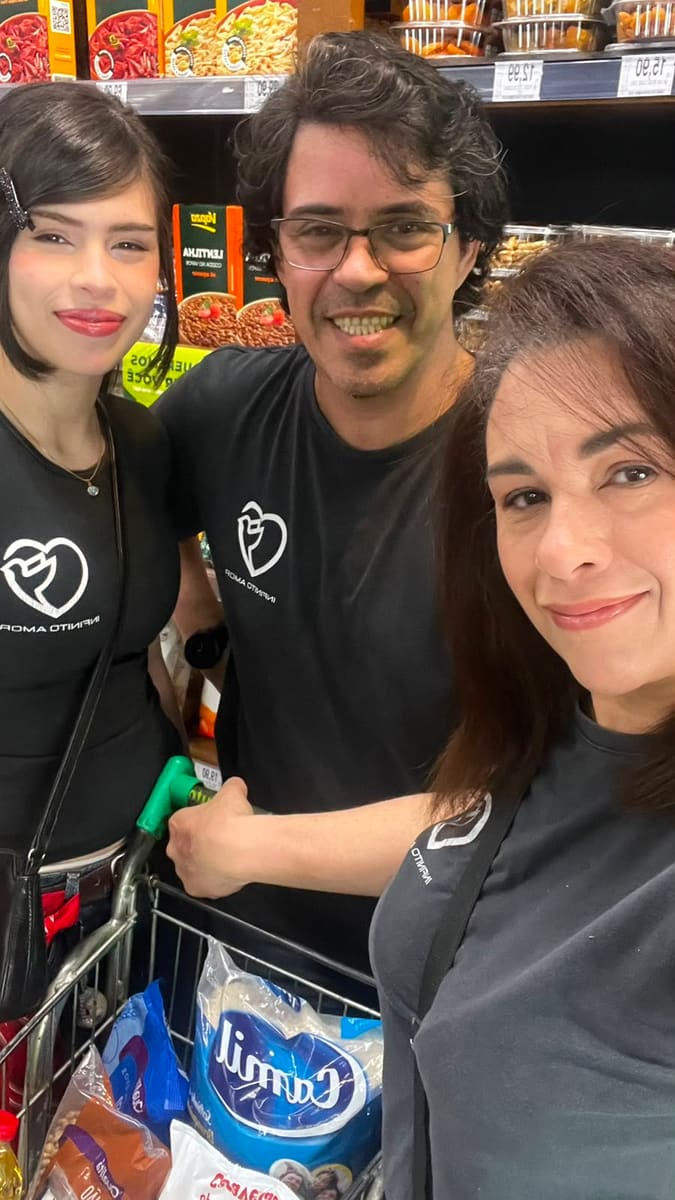 Três voluntários da Infinito Amor com camisetas da igreja no supermercado, com o carrinho carregado de alimentos durante a campanha de arrecadação.