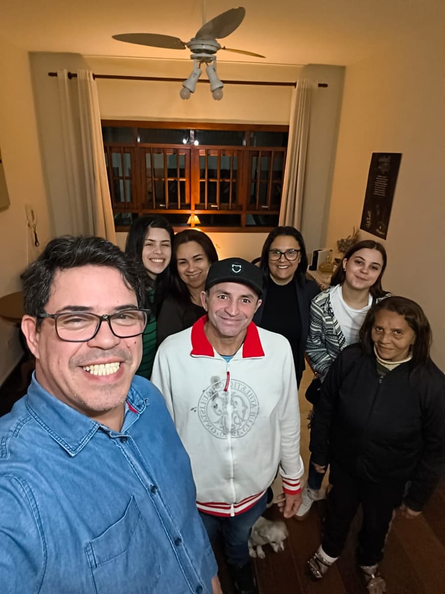 Grupo reunido na sala de uma casa, sorrindo, no Estudo Bíblico da Família Infinito Amor.