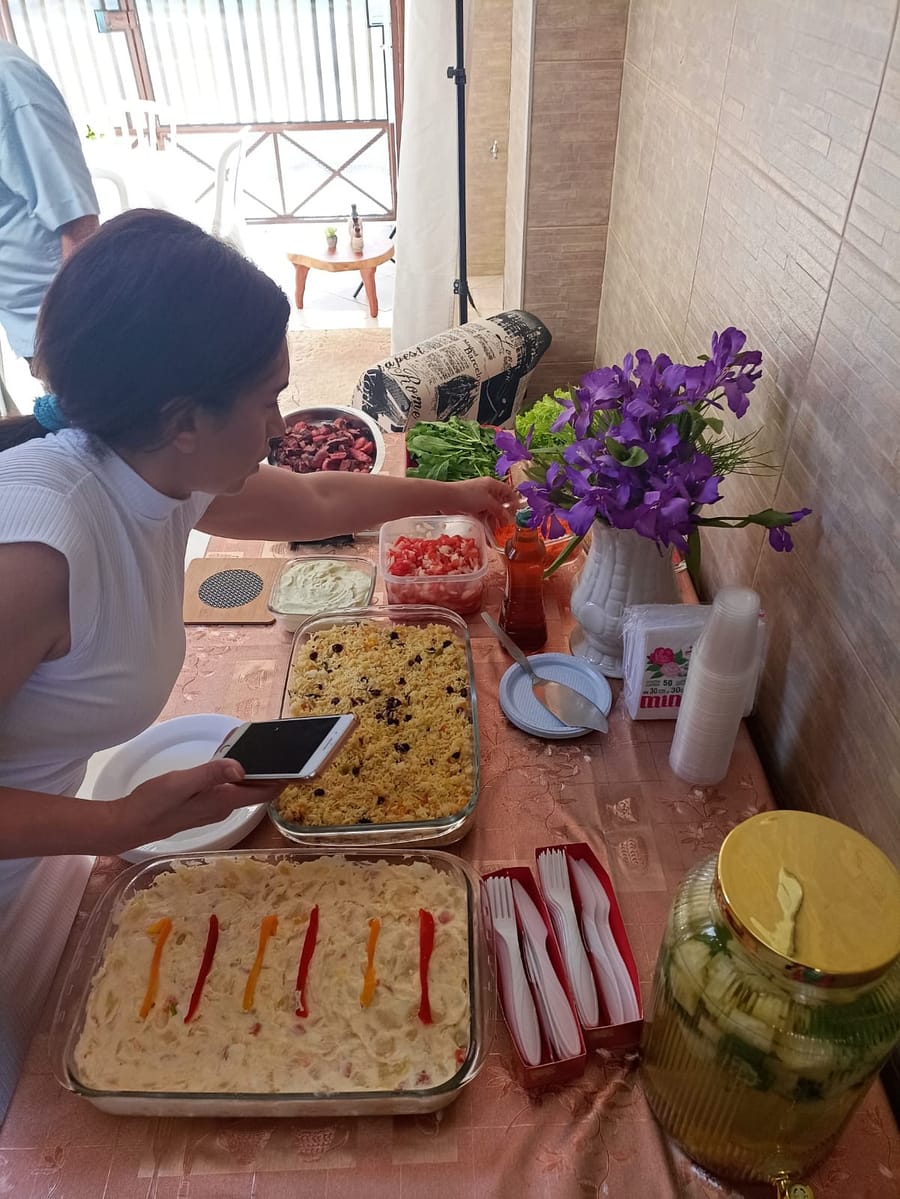 A Pra. Patrícia preparando a mesa da confraternização, com travessas de comida, copos e flores.