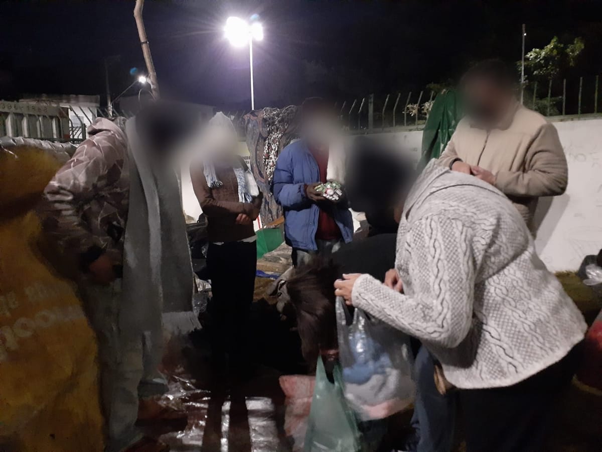Entrega noturna de marmitas e agasalhos a pessoas em situação de rua. Os rostos foram desfocados.