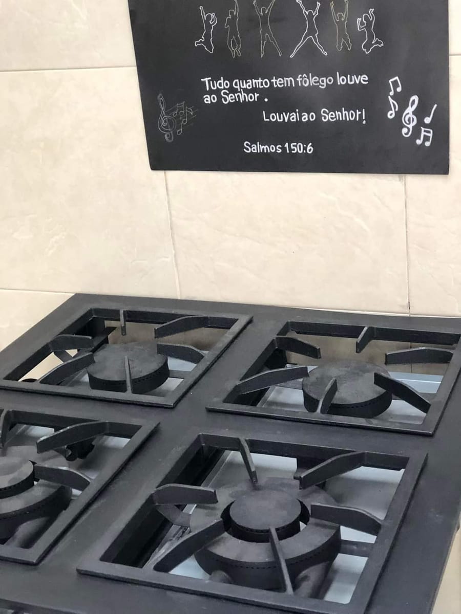 Fogão industrial de quatro bocas doado para a cozinha, com um cartaz do Salmo 150:6 na parede.